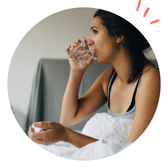 Dame sitter i sengen med medisiner og et glass vann.