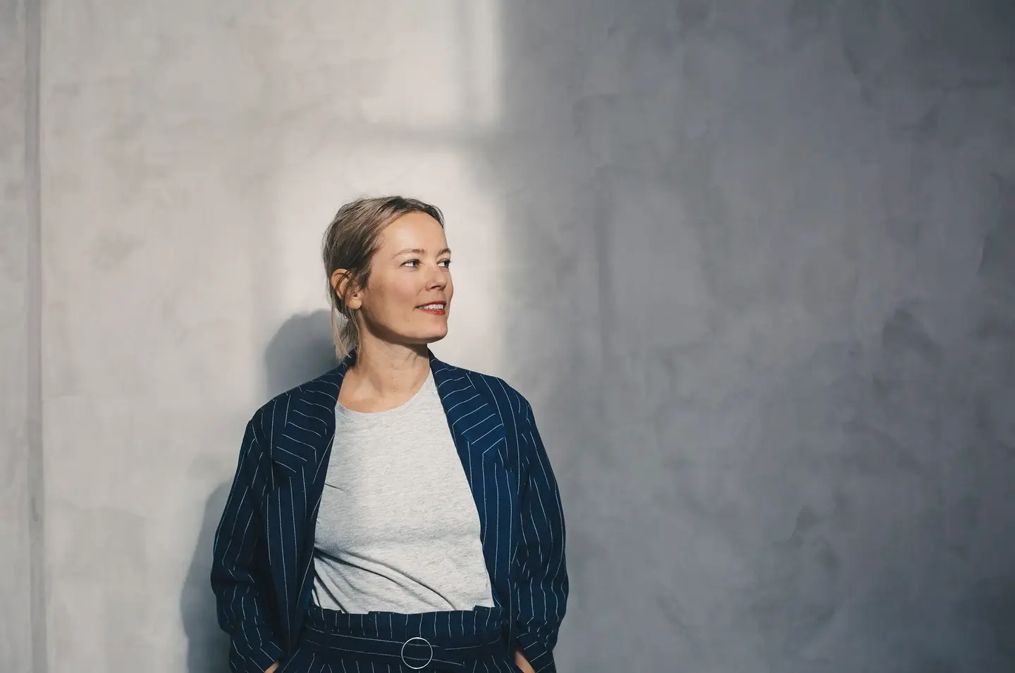 Ung forretningskledd person med hendene i lommene og et smil om munnen.